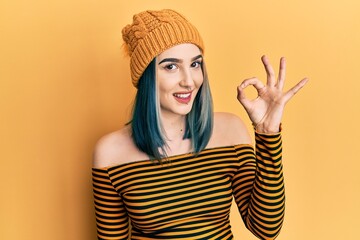 Young modern girl wearing wool hat smiling positive doing ok sign with hand and fingers. successful expression.