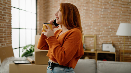 Young redhead woman talking on the smartphone drinking coffee at new home