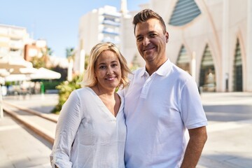 Middle age man and woman couple hugging each other standing at street