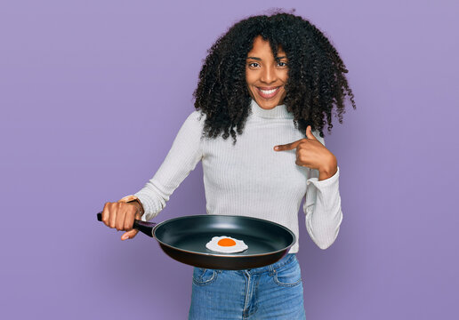 Young african american girl holding skillet with fried egg pointing finger to one self smiling happy and proud