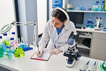 Young hispanic woman wearing scientist uniform listening to music working at laboratory