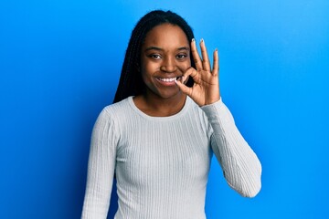 African american woman with braided hair wearing casual white sweater smiling positive doing ok sign with hand and fingers. successful expression.