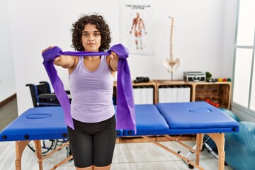 Fototapeta premium Young hispanic woman doing rehabilitation using elastic band at clinic