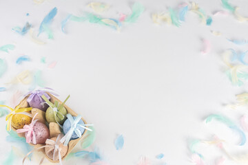 Easter colored eggs in a box, on a white background decorated with colored feathers. There is space for text. View from above