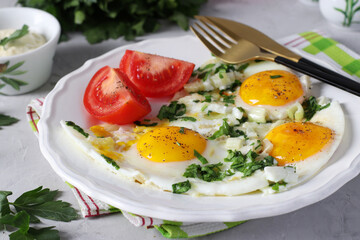 Fried eggs with celery and parsley on a white plate, served with tomatoes. Healthy and tasty breakfast