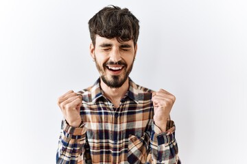 Hispanic man with beard standing over isolated background excited for success with arms raised and eyes closed celebrating victory smiling. winner concept.
