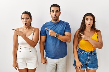 Fototapeta premium Group of young hispanic people standing over isolated background surprised pointing with finger to the side, open mouth amazed expression.