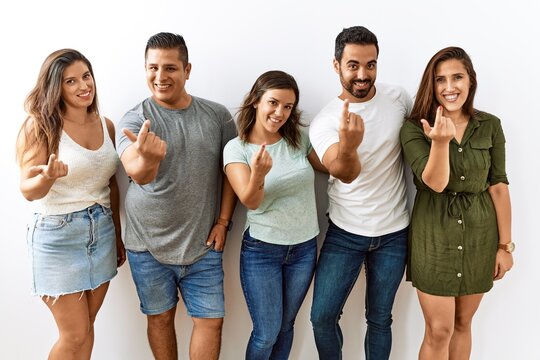 Group of young hispanic friends standing together over isolated background beckoning come here gesture with hand inviting welcoming happy and smiling