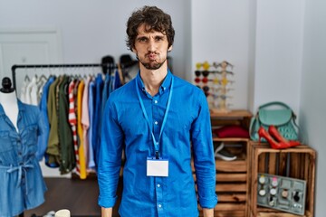Young hispanic man working as manager at retail boutique puffing cheeks with funny face. mouth...