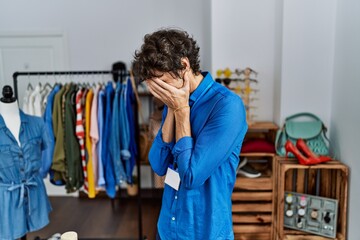 Young hispanic man working as manager at retail boutique with sad expression covering face with...