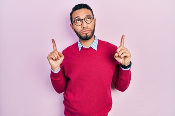 Hispanic man with beard wearing business shirt and glasses pointing up looking sad and upset,...