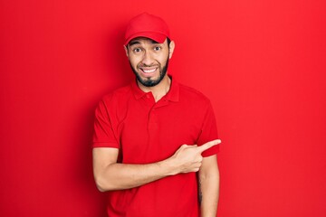 Hispanic man with beard wearing delivery uniform and cap pointing aside worried and nervous with...