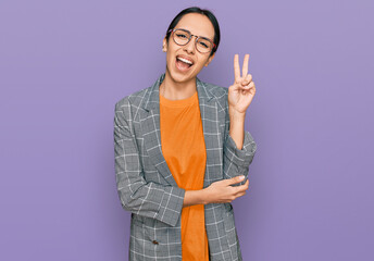 Young hispanic girl wearing business jacket and glasses smiling with happy face winking at the...