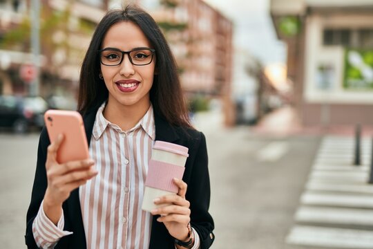 Young hispanic businesswoman using smartphone drinking coffee at the city.