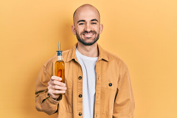 Young bald man holding olive oil can looking positive and happy standing and smiling with a...