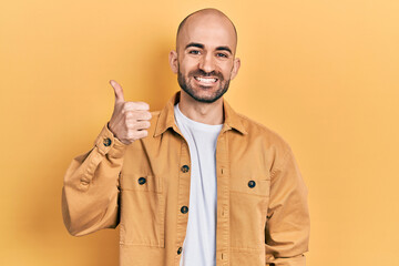 Young bald man wearing casual clothes smiling happy and positive, thumb up doing excellent and approval sign