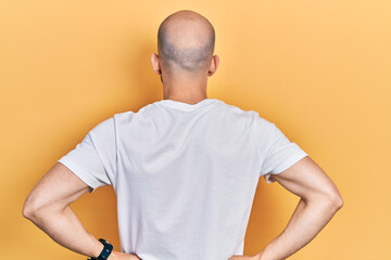 Young bald man wearing casual white t shirt standing backwards looking away with arms on body