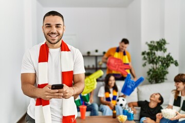 Group of young friends watching and supporting soccer match. Man smiling happy using smartphone at home.