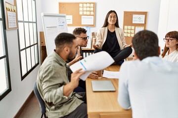 Businesswoman enjoys meditating during meeting. Sitting on desk near arguing partners at the office.