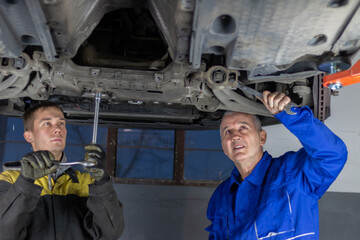 A senior experienced technician helps a young fellow mechanic fix the car