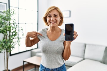 Middle age blonde woman working holding smartphone showing screen pointing finger to one self smiling happy and proud