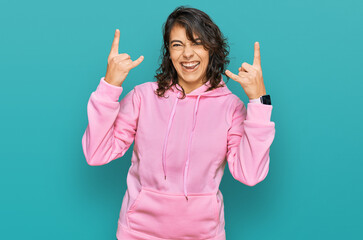 Young hispanic woman wearing casual sweatshirt shouting with crazy expression doing rock symbol with hands up. music star. heavy music concept.