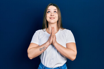 Young hispanic girl wearing casual white t shirt begging and praying with hands together with hope...