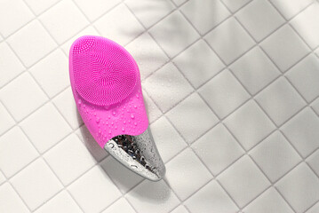 Pink facial sonic brush for massage on white tile with water drops