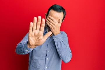 Middle age hispanic man wearing casual clothes covering eyes with hands and doing stop gesture with sad and fear expression. embarrassed and negative concept.