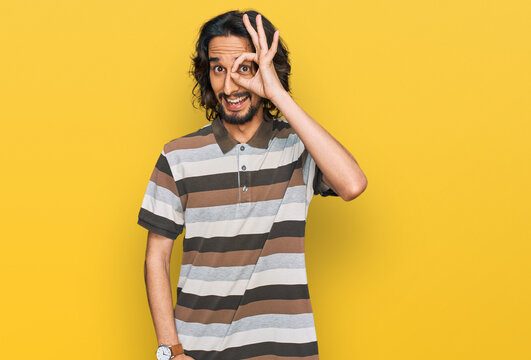 Young hispanic man wearing casual clothes doing ok gesture with hand smiling, eye looking through fingers with happy face.