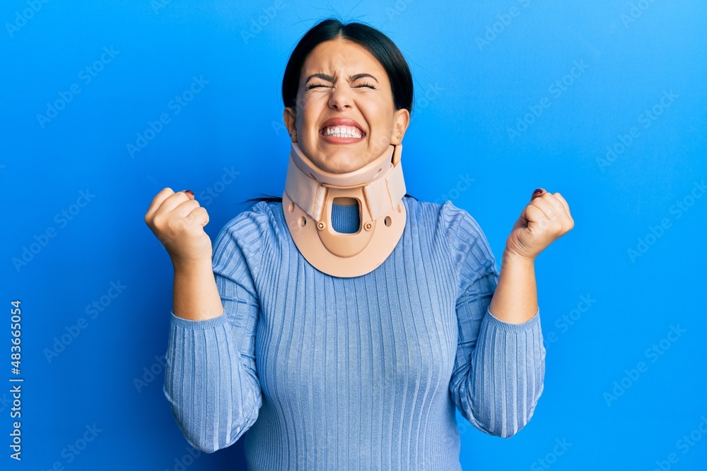 Sticker beautiful brunette woman wearing cervical collar very happy and excited doing winner gesture with ar