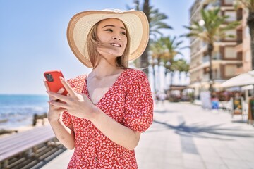 Fototapeta premium Young chinese girl wearing summer hat using smartphone at the promenade.