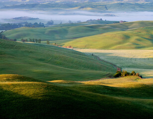 Fototapeta na wymiar Spring Tuscany. View of the sunlit hills. There is fog in the valley.