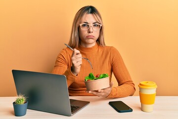 Young caucasian woman working at the office eating healthy salad depressed and worry for distress, crying angry and afraid. sad expression.