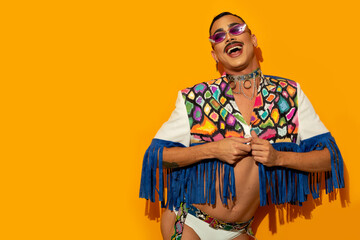 Portrait of happy young drag queen laughing in a colorful dress on a yellow background