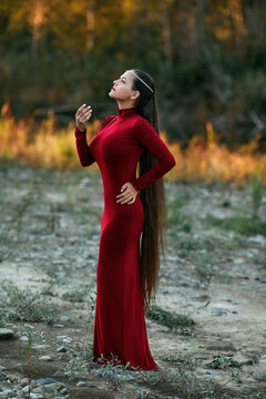 Long hair woman in red dress posing in autumn park on sunset. Fashion young russian lady in outdoor walk