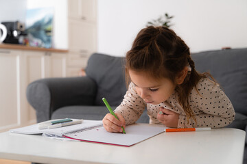 Portrait of cute preschooler child girl drawing with pencils at home while sitting in front of the...