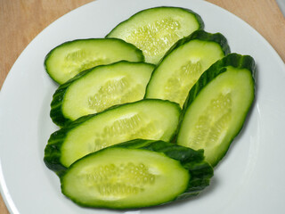  A smooth, medium-sized cucumber cut into slices. Cucumber on a plate. Vegetable isolate. Fresh ripe vegetable