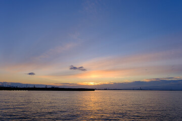 Fototapeta na wymiar 早朝、朝日にキラキラ輝き、黄金色に輝く海。兵庫県芦屋市芦屋浜より大阪湾を臨む。遠くに大阪南港のビルが見える