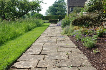 Fototapeta na wymiar Scenic View of a Stone Path Way Lined by Plants and Flowers in a Beautiful English Style Formal Garden