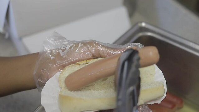 chica joven  colocandole hot dog al pan, comida rapida en casa.