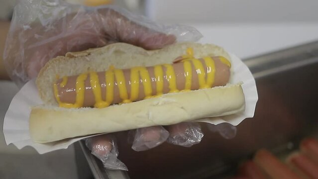 chica joven con hot dog en mano colocandole queso derretido encima del hot dog, comida rapida en casa.