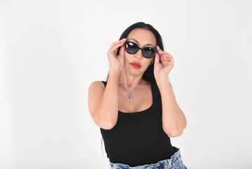 Stylish woman in the studio on a white background in sunglasses, jeans and a black T-shirt