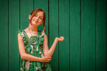 Teen girl portrait in a dress on a green background. Girl 10 or 11 years old on a summer day.