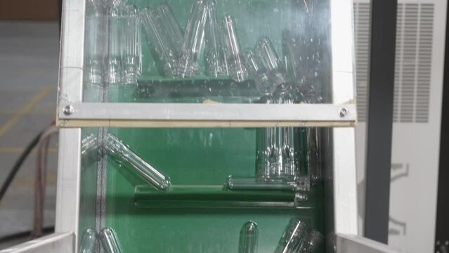 A close-up view of transparent PET preforms being transported by an elevator into a blowing machine