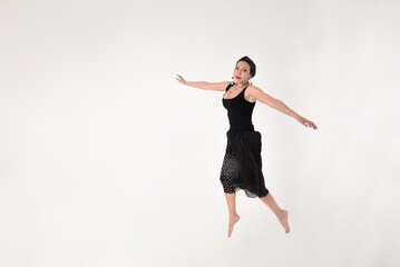 A brunette woman in a black dress barefoot jumped into the air in delight on a white background