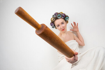 Funny woman in home style. Woman with wooden rolling pin in her hands. Girl in bath towel waves...
