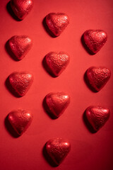 Closeup of heart shaped chocolate confections, and red roses against a bright red background.