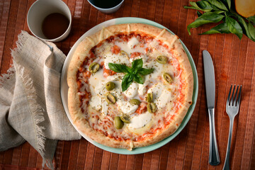 Italian pizza with olives, mozzarella and tomato on wooden table