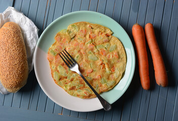 omelette with carrots and zucchini in the big plate with the bread beside it